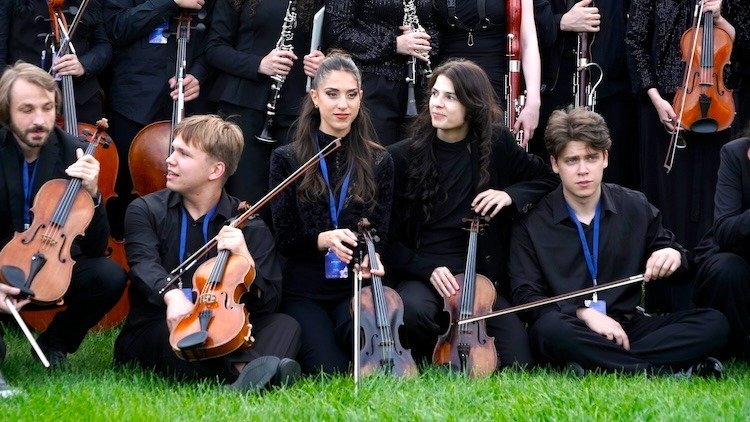 WhatsApp Image 2026-08-29 at 123203 PM 5 - عروبة الاخباري | Oroba News Group of young violinists in black, sitting on grass with their instruments.