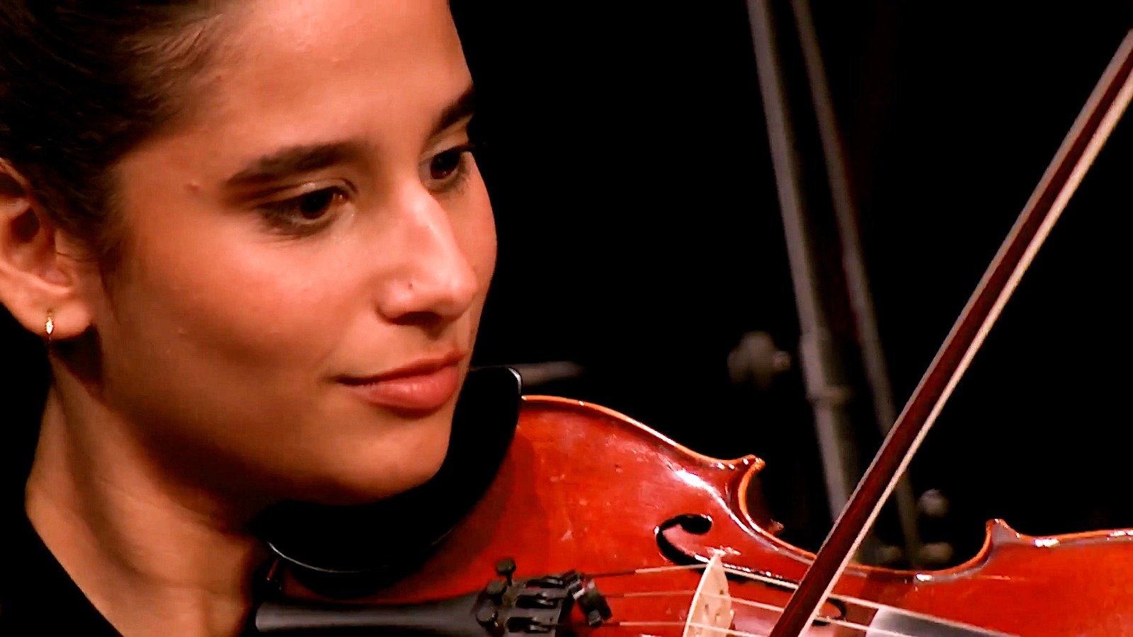 WhatsApp Image 2026-08-29 at 123204 PM 3 - عروبة الاخباري | Oroba News Close-up of a woman playing a violin, focused on her face and the instrument with bow drawn across strings.