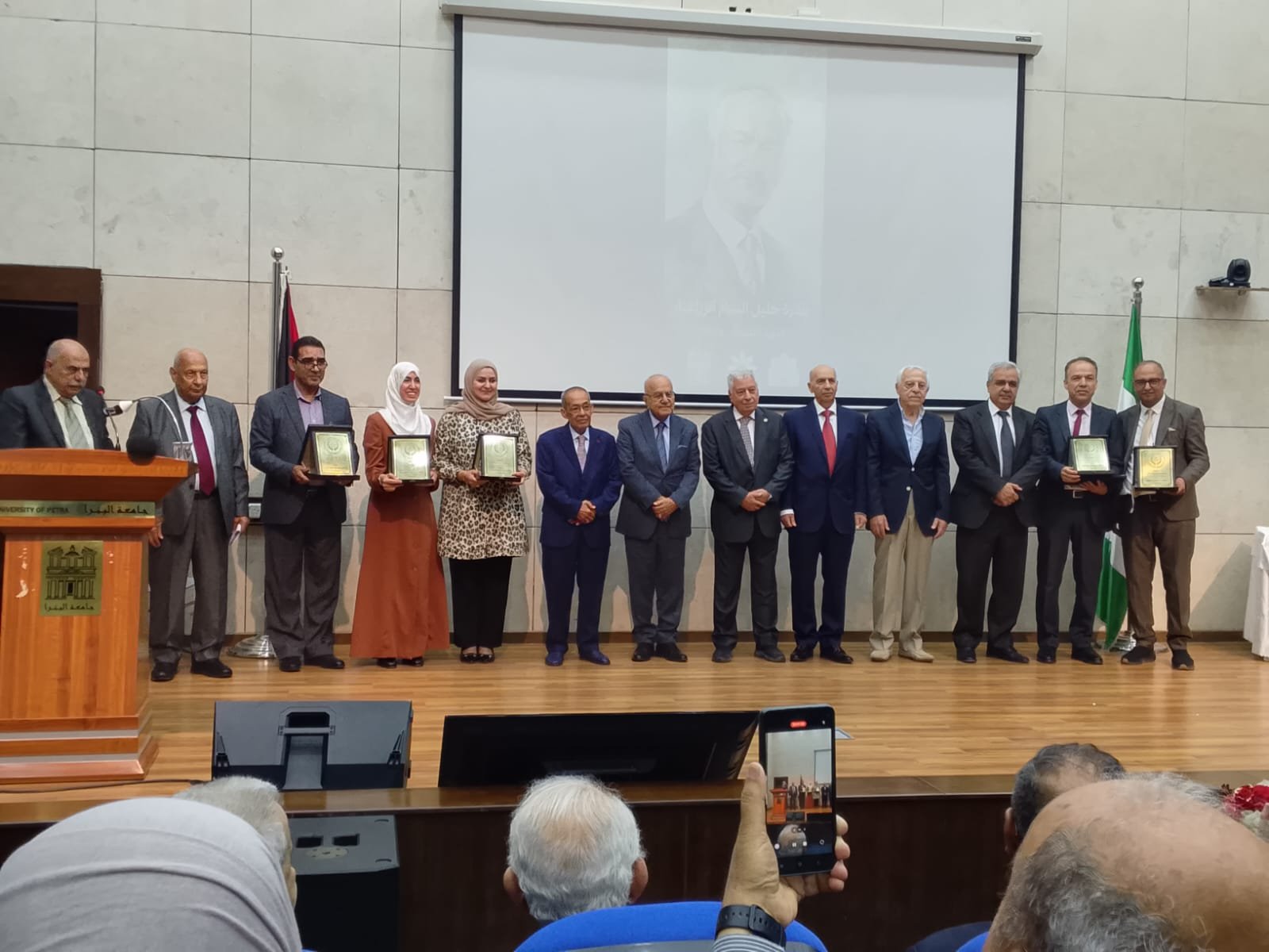 WhatsApp Image 2026-08-29 at 43333 PM - عروبة الاخباري | Oroba News Group of men and women in formal attire on stage receiving plaques at a university ceremony.