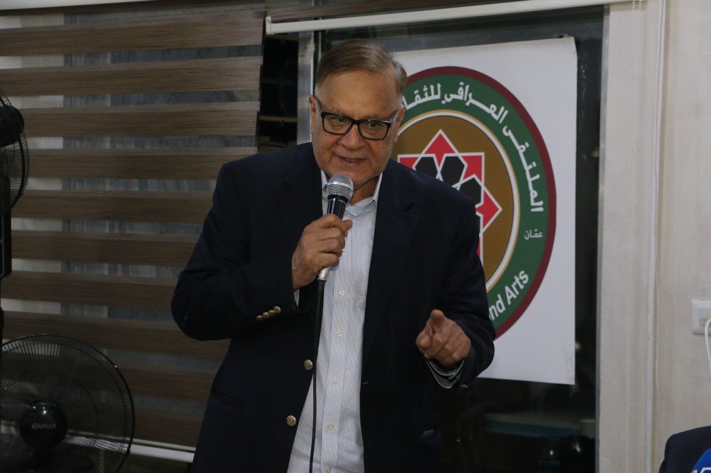 WhatsApp Image 2026-08-31 at 122517 AM - عروبة الاخباري | Oroba News Older man in a navy blazer and glasses speaks into a microphone at an arts event, with a circular banner behind him.