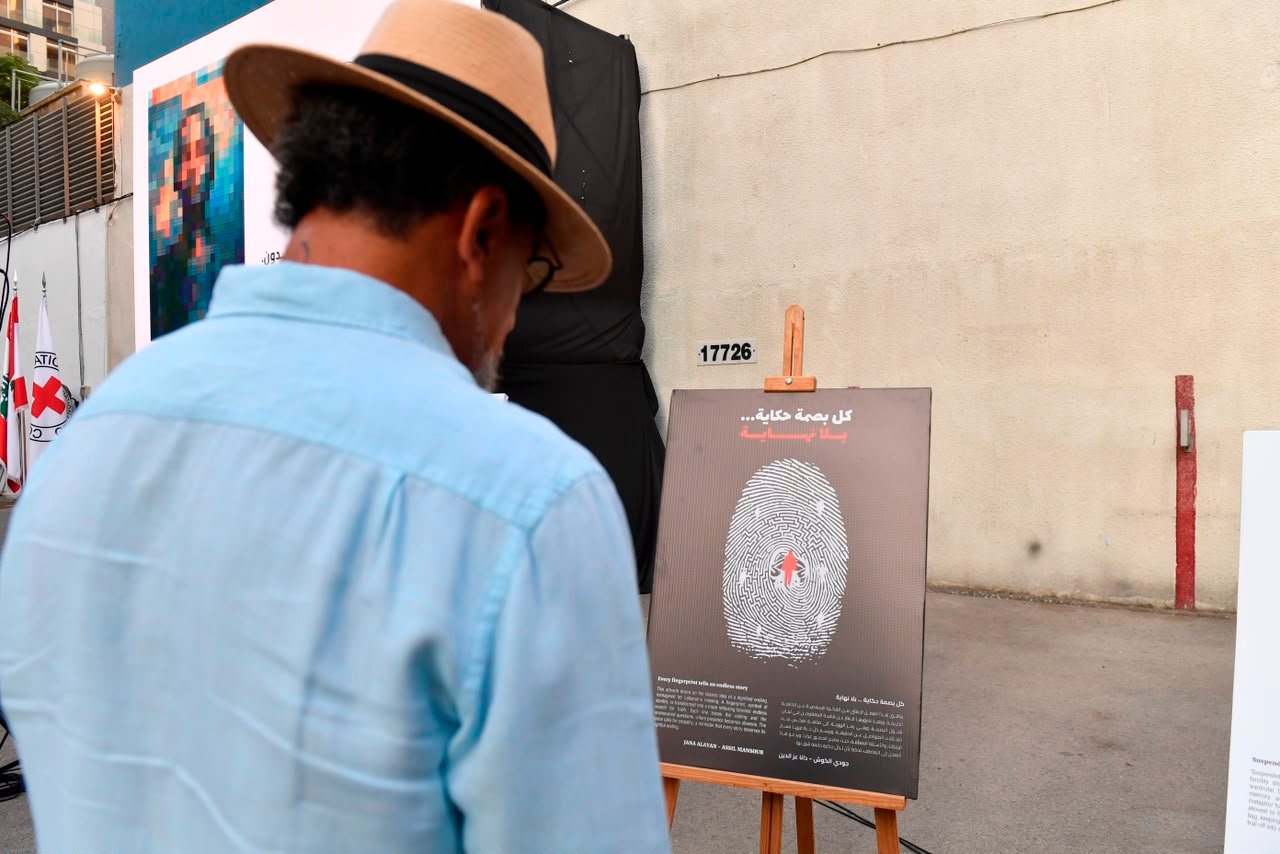 Man in a light blue shirt and fedora reads a fingerprint-themed poster at an outdoor exhibit.
