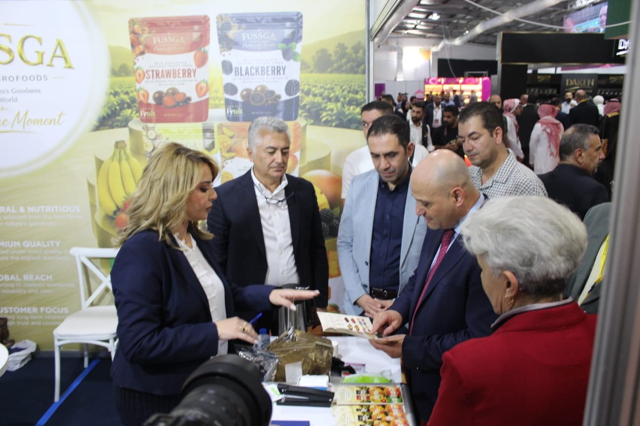 Group of professionals at a trade fair booth examining product samples in front of a large fruit snack backdrop.