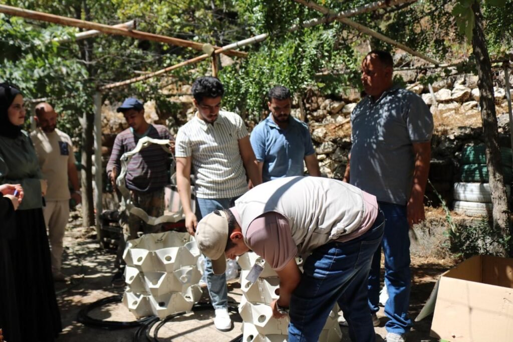 Group of men outdoors watching a man bend over white geometric components on the ground for assembly.