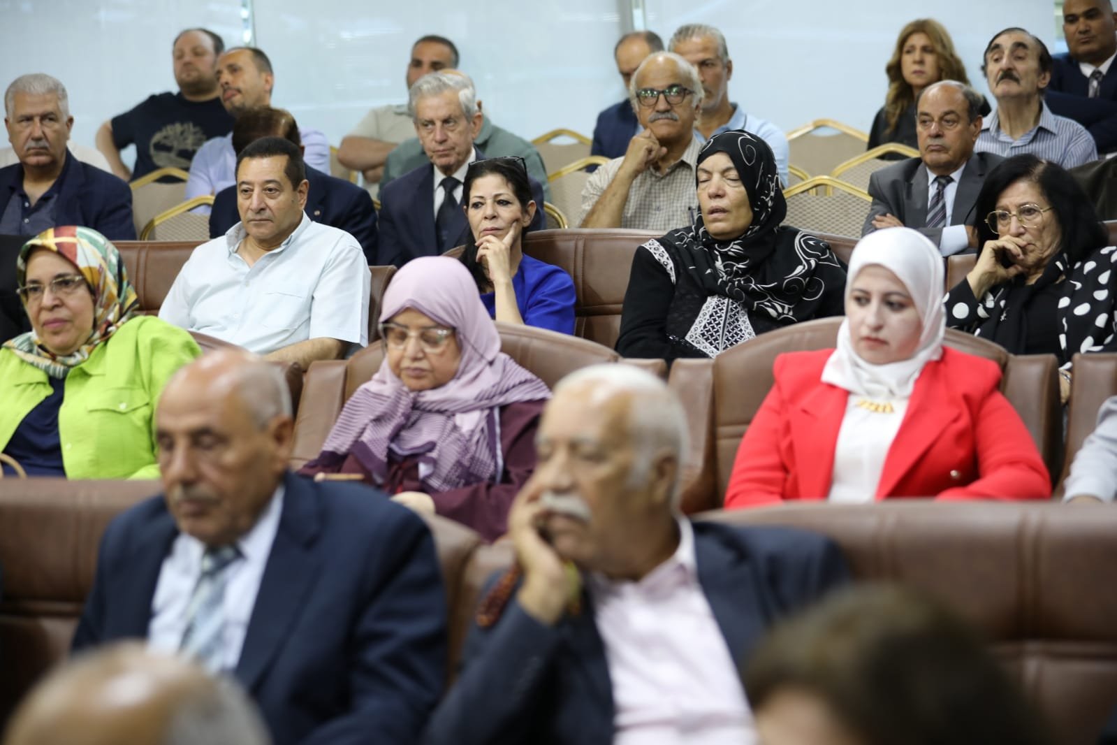 Audience of diverse adults seated in a conference room, attentive to a presentation.