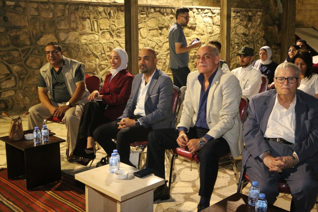 WhatsApp Image 2026-09-07 at 122850 AM - عروبة الاخباري | Oroba News Group of men and women seated in a stone-walled venue, dressed in business casual attire, attending a formal event.