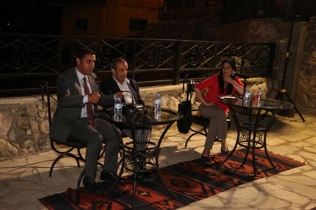 WhatsApp Image 2026-09-07 at 122856 AM - عروبة الاخباري | Oroba News Panel discussion outdoors at night with three speakers seated at glass tables, microphones in use and water bottles nearby.
